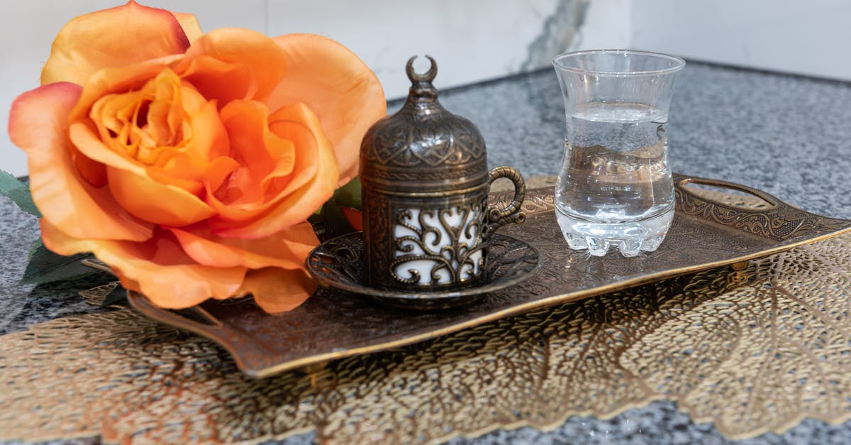 Use of traditional copper sauteuse pans - Metal authentic Turkish coffee mug with plate placed on tray with cup of water and big rose on table in room