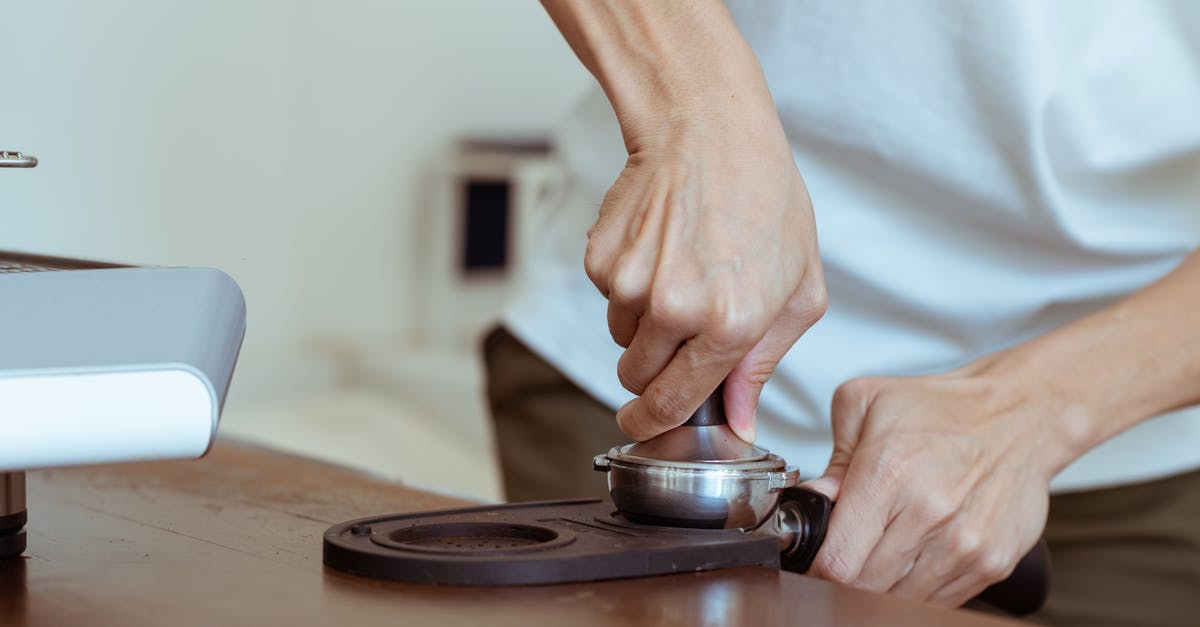 Using a French press with finely ground coffee - Crop anonymous cafe employee in white tee using tamper to press freshly ground morning coffee in portafilter