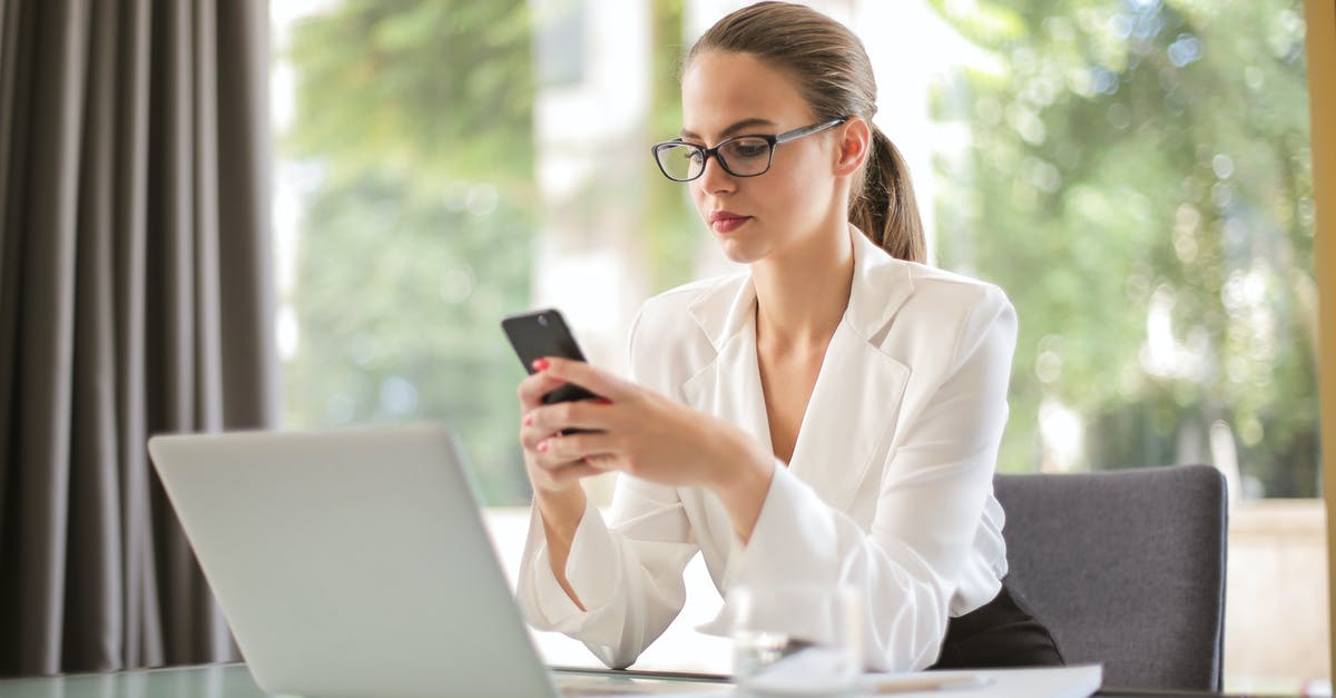 Using cast iron on a glass range - Concentrated young woman in formal clothes and eyeglasses sitting at glass table with laptop while surfing smartphone