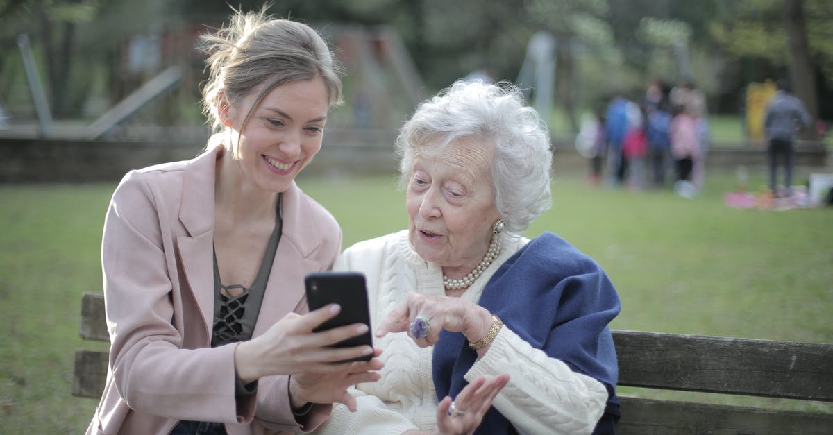 Using old vanilla beans - Delighted female relatives sitting together on wooden bench in park and browsing mobile phone while learning using