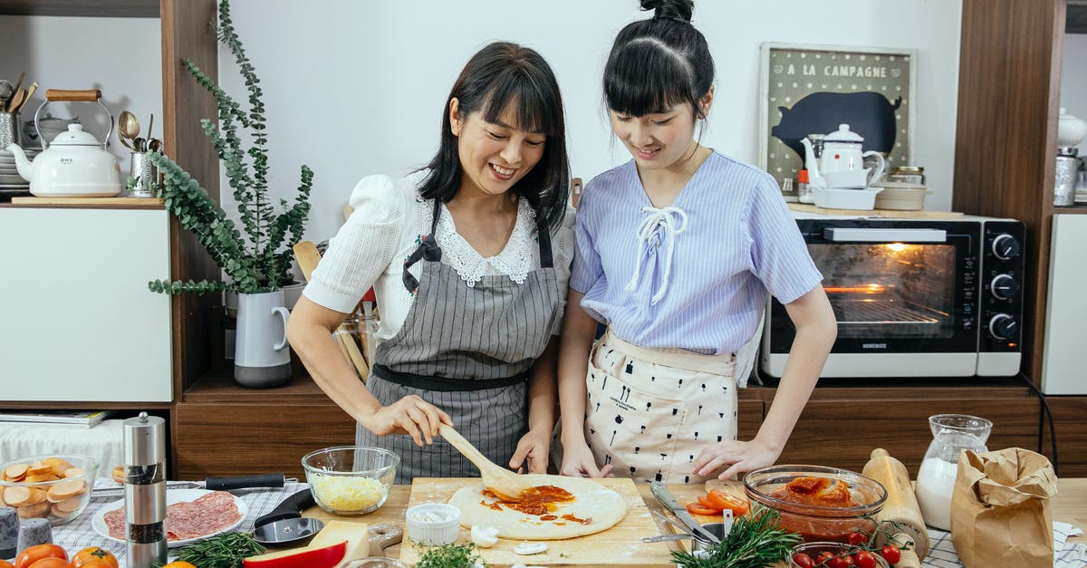 Using over-rested pizza dough as old dough - Cheerful women spreading sauce on pizza dough