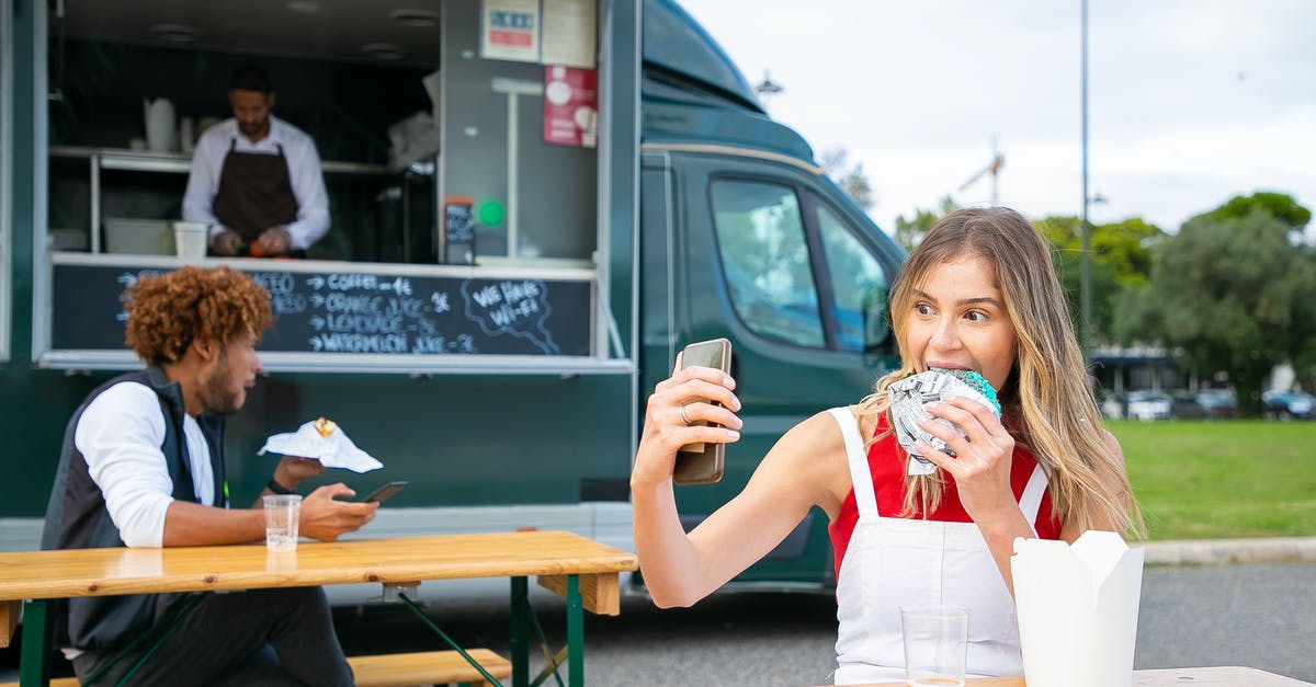 using polenta to make hamburger - Cheerful young woman in casual clothes eating delicious blue burger and taking selfie while chilling on street near food truck with busy owner and black man eating hamburger in daytime
