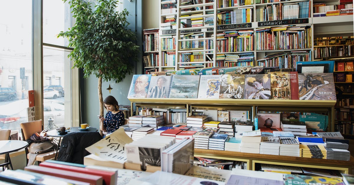 Using salmon in 2 days, freezer or fridge? - Young female client in casual wear chatting on cellphone while sitting at table with cup of hot drink in cozy bookstore in afternoon