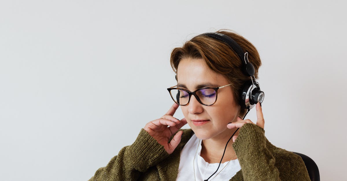 Using sous vide to warm canned vegetables - Content glad female wearing eyeglasses and headphones listening to good music and touching headset while sitting with eyes closed against white wall