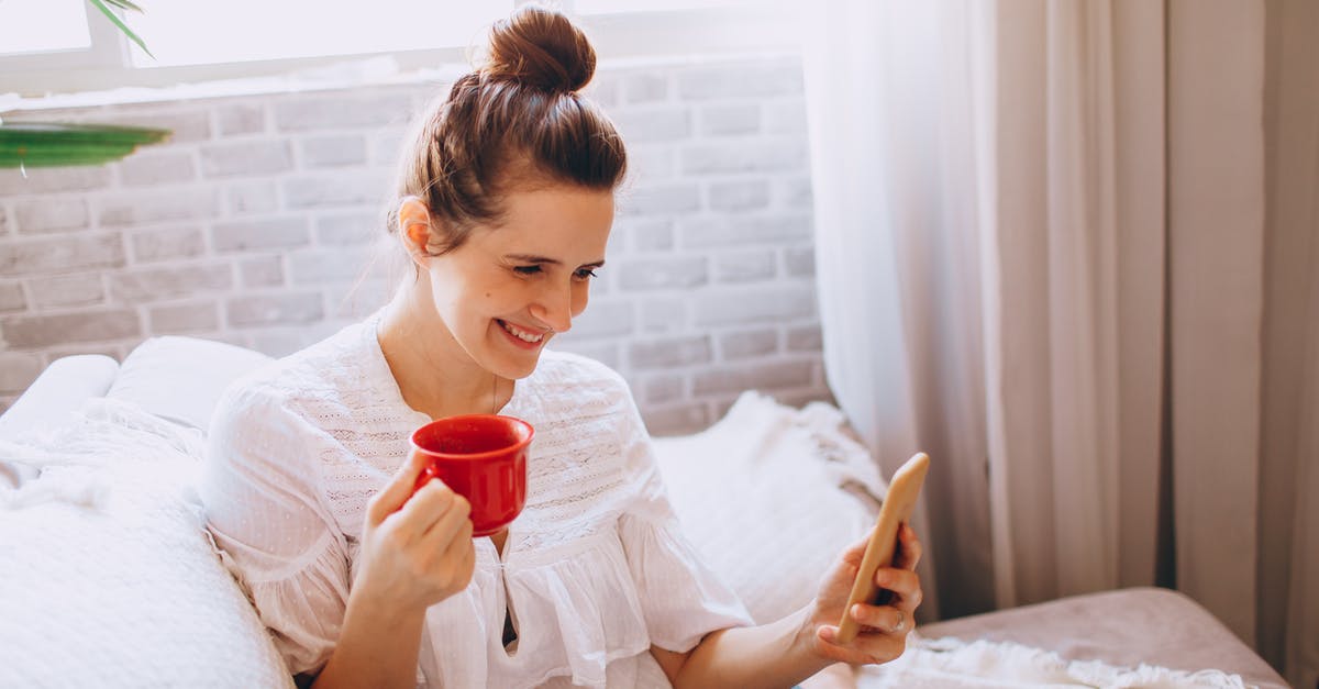 Using the right acid for red curry - Young cheerful female in casual clothes sitting on sofa and drinking coffee while using smartphone