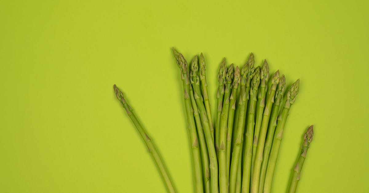 Vegetable similar to ivy gourd? - Overhead view of fresh asparagus stalks with wavy tips in row on smooth green surface