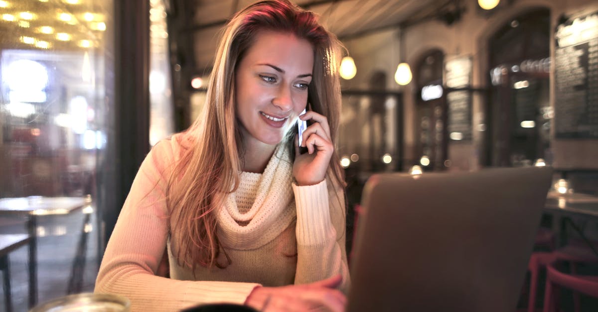 Warming refrigerated butter at a table in a restaurant - Content female wearing warm sweater sitting at table in cozy cafe and speaking on cellphone while resting in evening and browsing netbook