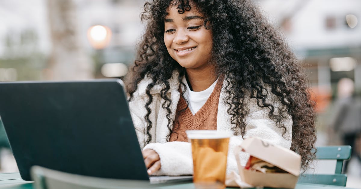 Warming refrigerated butter at a table in a restaurant - Smiling black woman using laptop in city park