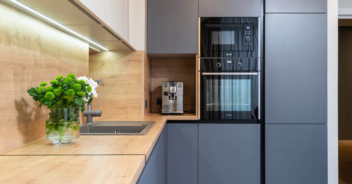 Water Exploded in Microwave - Creative design of kitchen with built in oven against coffee machine and flowers in vase on table in house