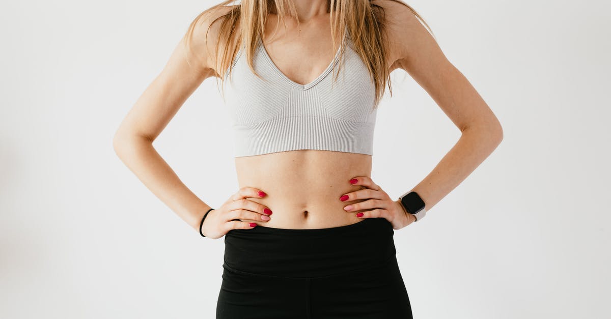 What's the black thing at the bottom of navel oranges? - Faceless slim anonymous blond female in sports bra and black leggings in wearable bracelet showing perfect belly on white background while standing with hands on waist