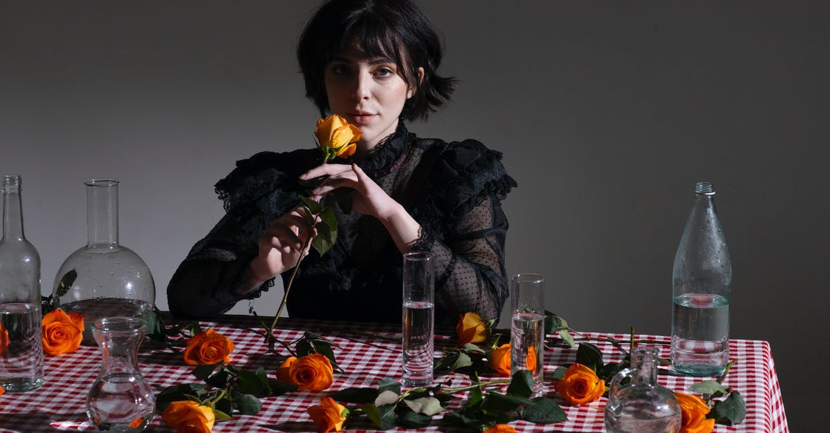 What's the difference between orange extract and orange blossom water? - Gothic female in black blouse at table with rose with orange petals on gray background