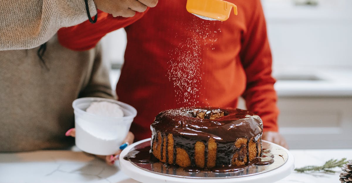 What actually happens if you pour a glaze over a loaf cake before it has cooled? - Crop ethnic parent with child decorating cake with icing sugar