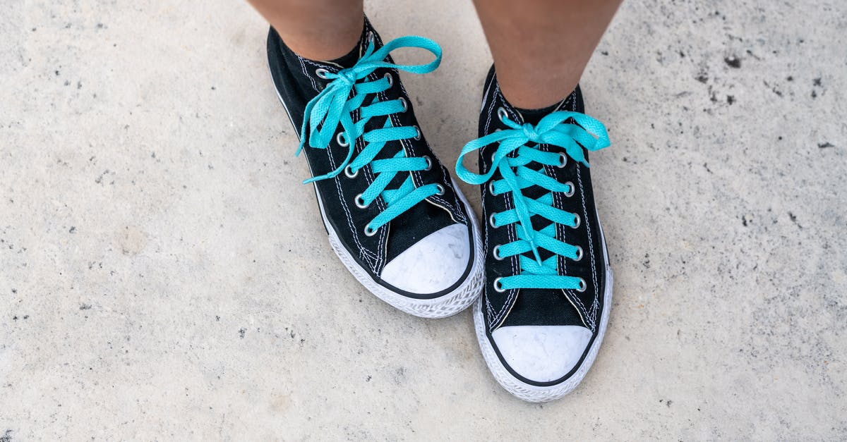 What are certified synthetic colors? - Top view of crop anonymous person in trendy footwear with blue shoelaces on gray background in daytime