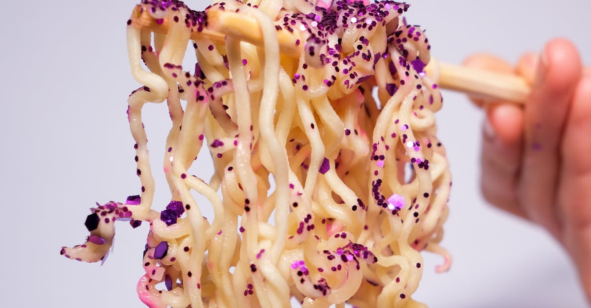What are examples of spoiled food that is part of a culture's cuisine? [closed] - Closeup of crop unrecognizable person holding instant noodles covered with sequins with chopsticks against gray background