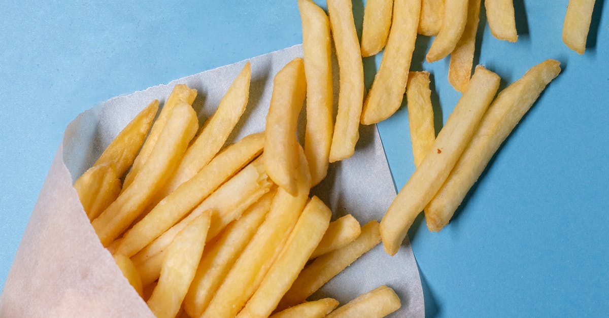 What are good counter-top oven settings to reheat french fries soggy from refrigerating overnight? - Top view of tasty french fries in paper placed on blue table in light studio