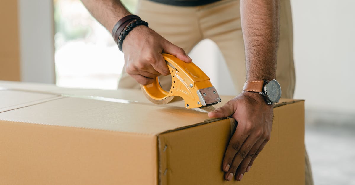 What are good techniques to prepare liver? - Crop faceless young male with wristwatch using adhesive tape while preparing cardboard box for transportation