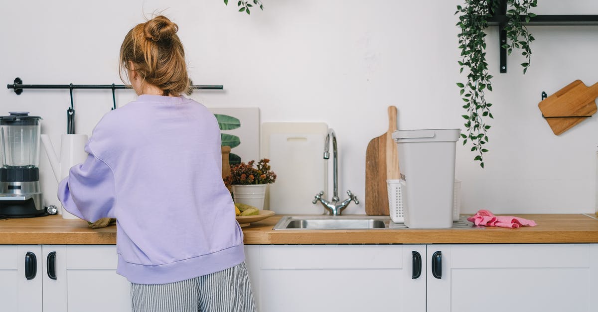 What are some recommended methods of cleaning wooden cutting boards? - Woman standing at wooden counter in kitchen in daytime