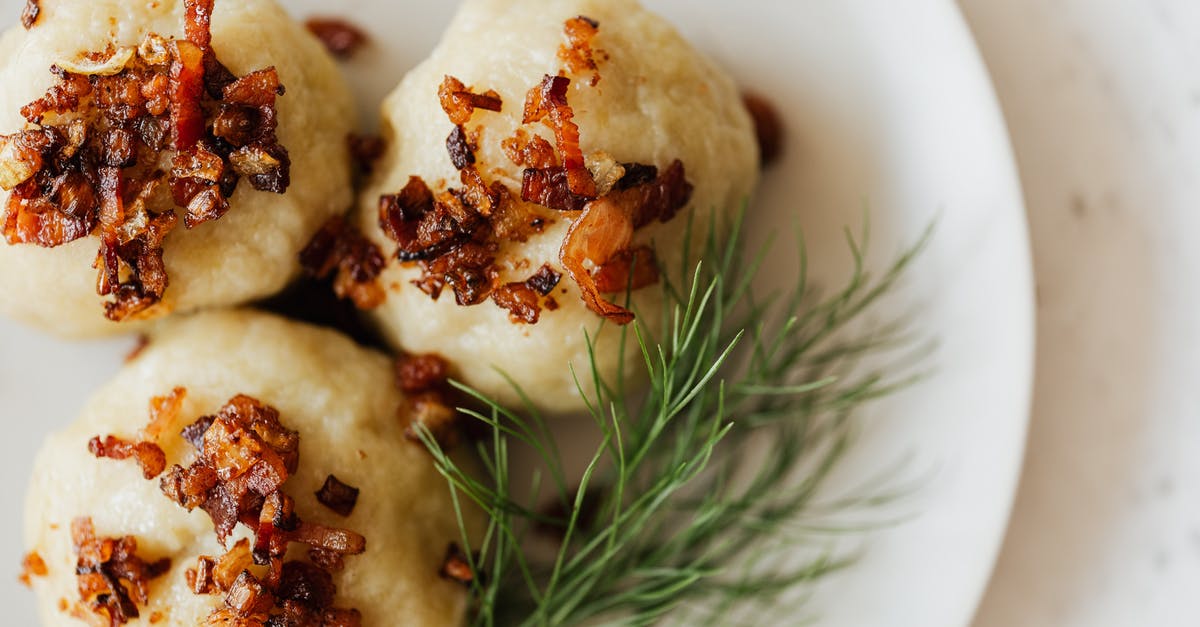 What are the crunchy bits on top of Thai mango with sticky rice? - Top view closeup of white ceramic plate with Lithuanian potato cepelinai with fried bacon bits on top and fresh dill sprig aside on marble table