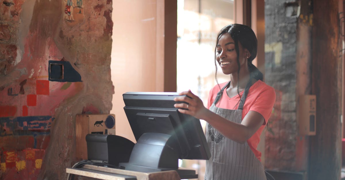 What are the major menu differences between Canadian and American Thanksgiving? - Cheerful American African waitress in apron working on counter monitor while registering order at cozy cafe