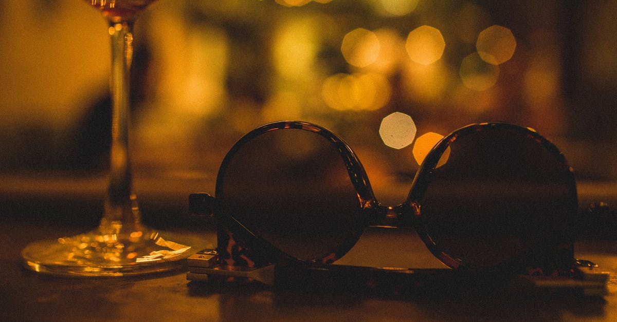 What are the natural and artificial sugars? - Composition of glass with refreshing drink on thin leg near modern sunglasses for women in plastic frame on wooden table in restaurant at night