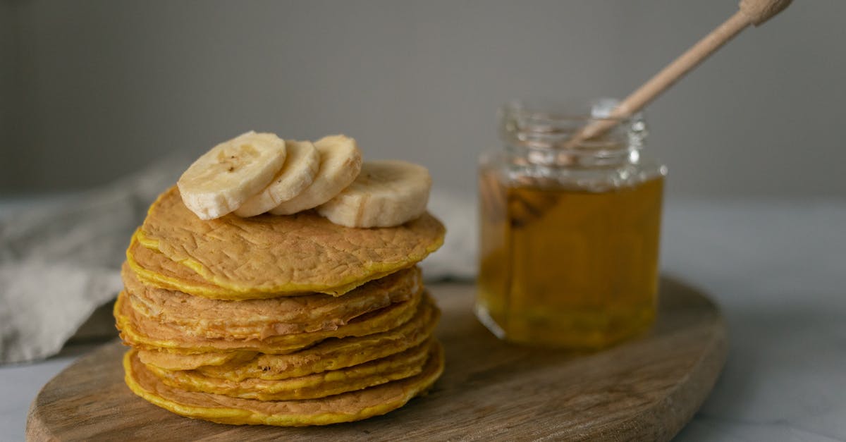 What can replace milk, for vegan pancakes without eggs? - Tasty homemade pancakes with sliced bananas near jar with honey and wooden spoon on cutting board on table