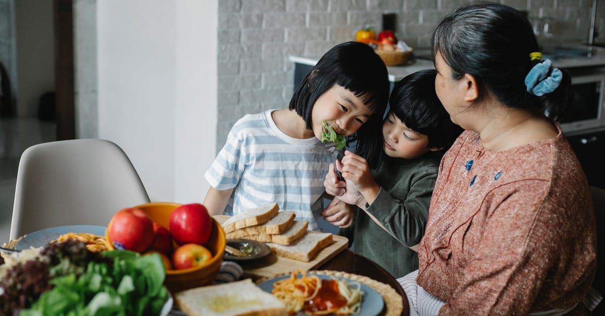 What characteristics should a bread peel have? - Cheerful little Asian siblings feeding each other while having lunch together with happy grandmother in modern kitchen