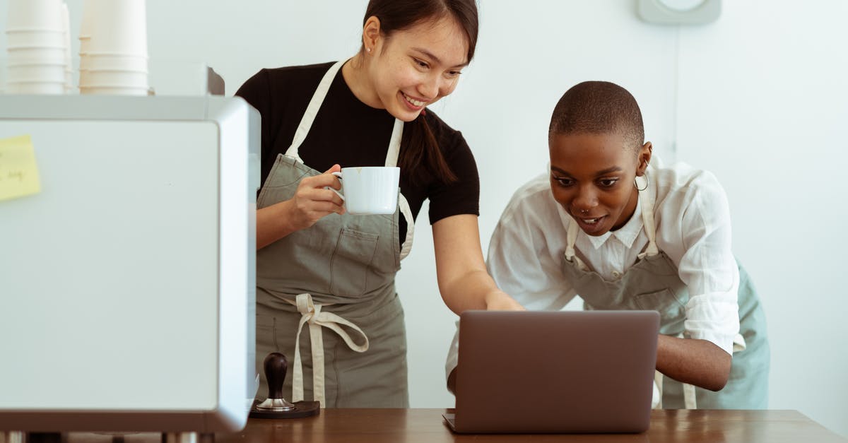 What cooking gadget is that? - Joyful smiling multiracial waitresses surfing internet on contemporary netbook and smiling while having coffee break in cozy kitchen