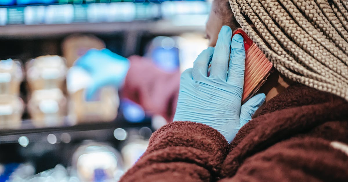 What do you call it and where to buy some - Side view of crop African American female customer in latex gloves with braids having phone call while picking food from shelf in grocery store