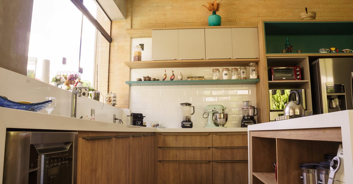 What does a fridge do apart from storing and cooling? - From below wooden cabinets and shelves of cozy kitchen with stainless steel appliances in sunlight