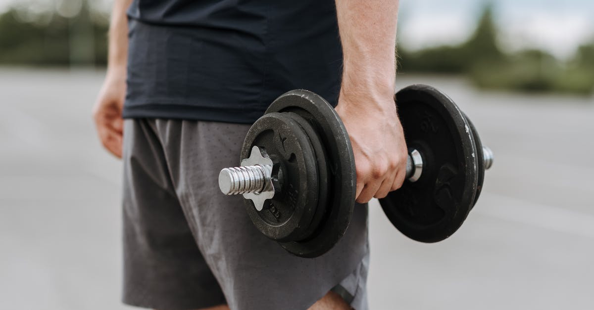 What does a healthy cast iron skillet look like? - Crop anonymous male in activewear lifting heavy iron dumbbell on blurred background of street