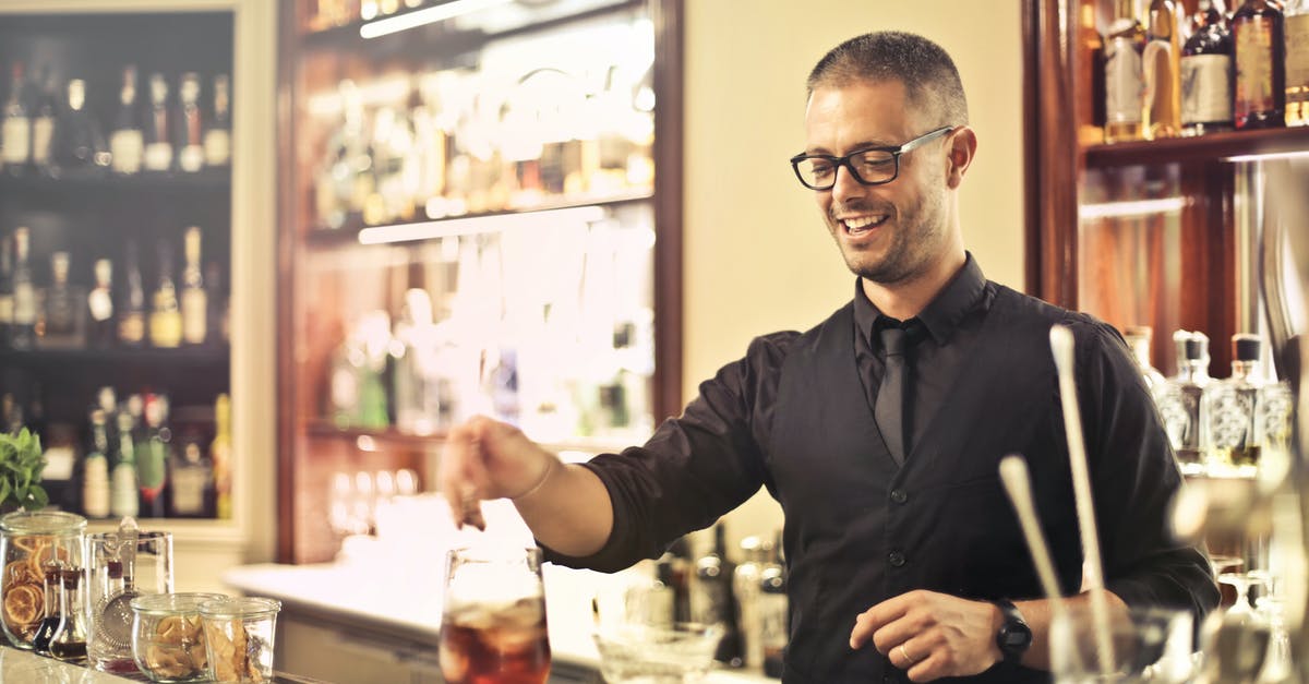 What happens when you mix whiskey and water? - Happy young male barkeeper standing at counter and preparing alcohol cocktail for order while working in modern pub