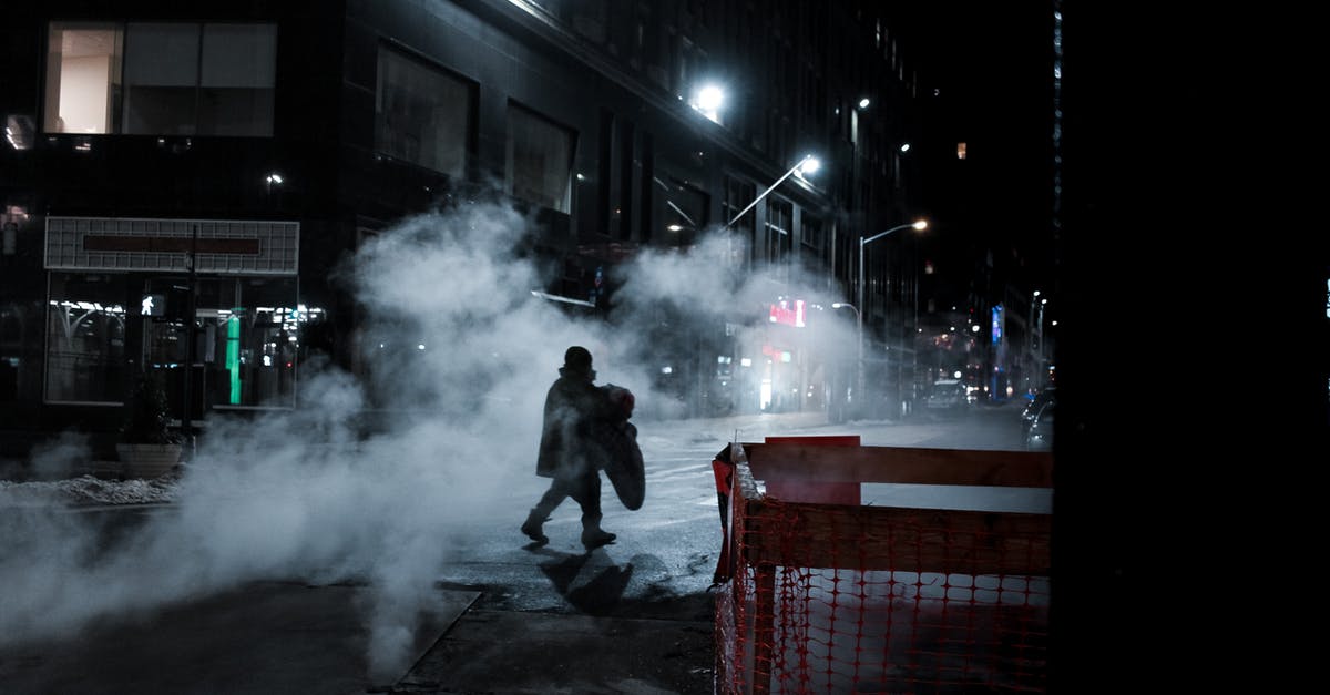 What is a good way to steam tamales without a "tamale steamer?" - Side view of distant anonymous person crossing asphalt roadway on street with steam and residential buildings at night time in city