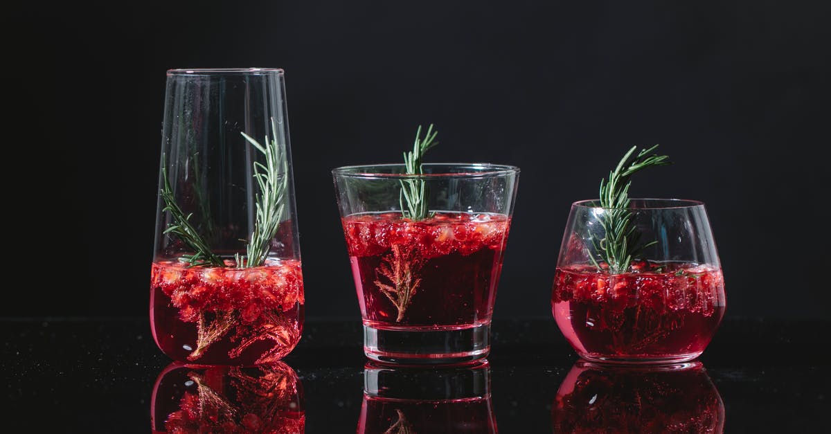 What is a liqueur? - Transparent clean glasses filled with similar red cocktail with rosemary and berries on black background