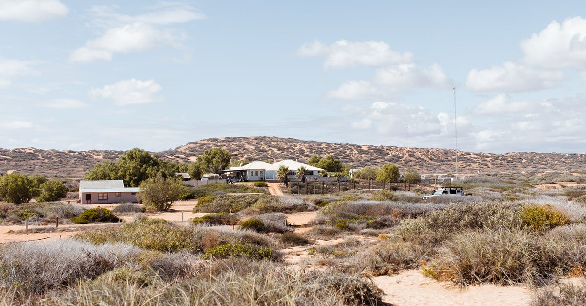 What is dry cottage cheese? - Distant buildings located on dry area with green shrubs against hills in semidesert terrain in rural settlement against cloudy sky