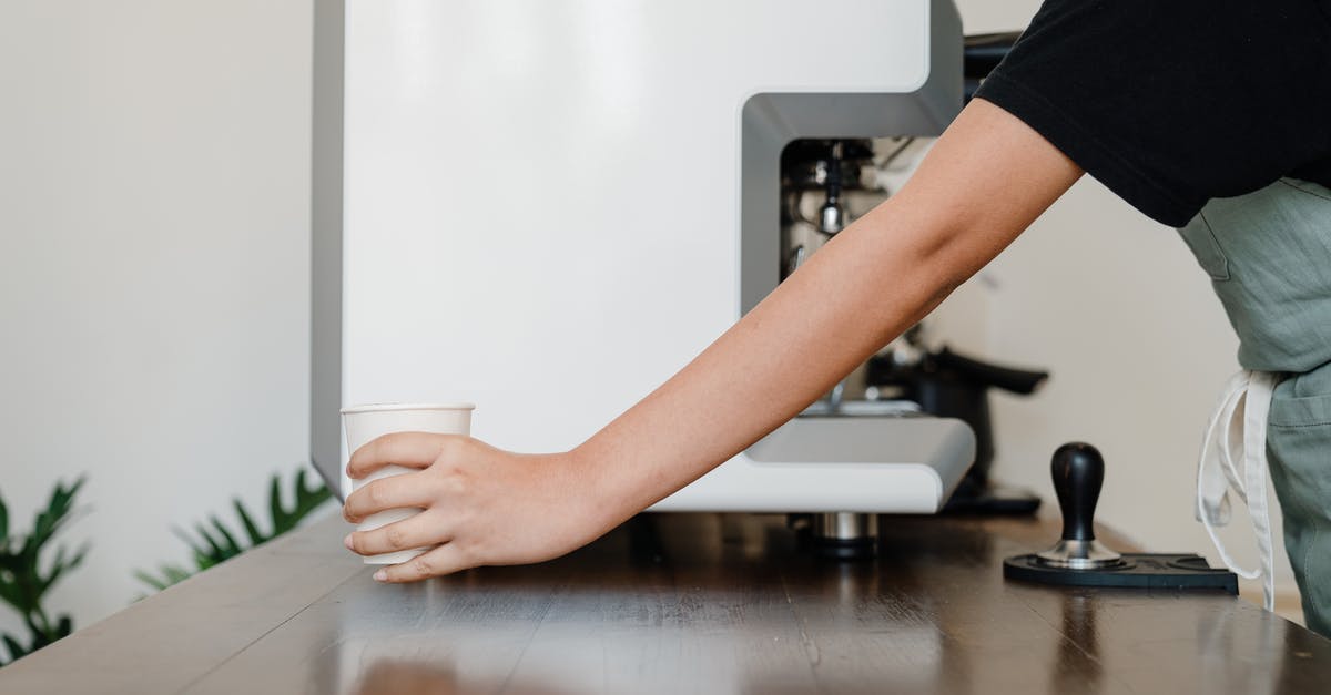 What is filter paper? - Crop unrecognizable female barista in black shirt and apron standing near modern professional coffee machine and passing white  takeaway paper cup with hot beverage across wooden table in coffee shop