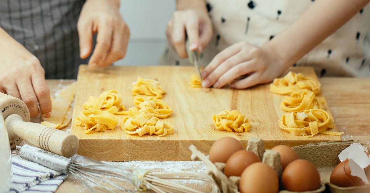 What is the best approach to cut carrot into thin strips? - Faceless females in aprons at wooden table making homemade pasta cutting dough into strips