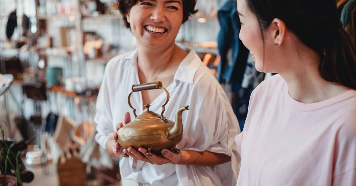 What is the best temperature to store honey at? - Crop cheerful ethnic female shoppers with oriental kettle speaking in local shop while spending time together and looking at each other