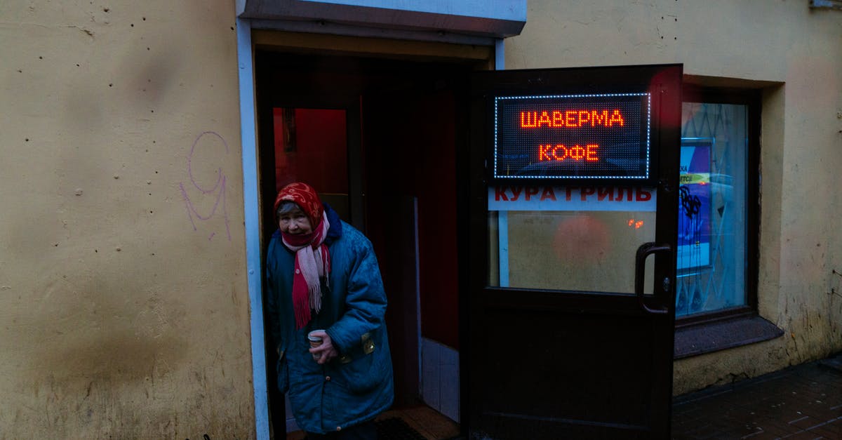 What is the best way to store ground coffee? - Senior gloomy female in shawl and warm jacket with cup of coffee leaning on entrance of bistro and looking at camera