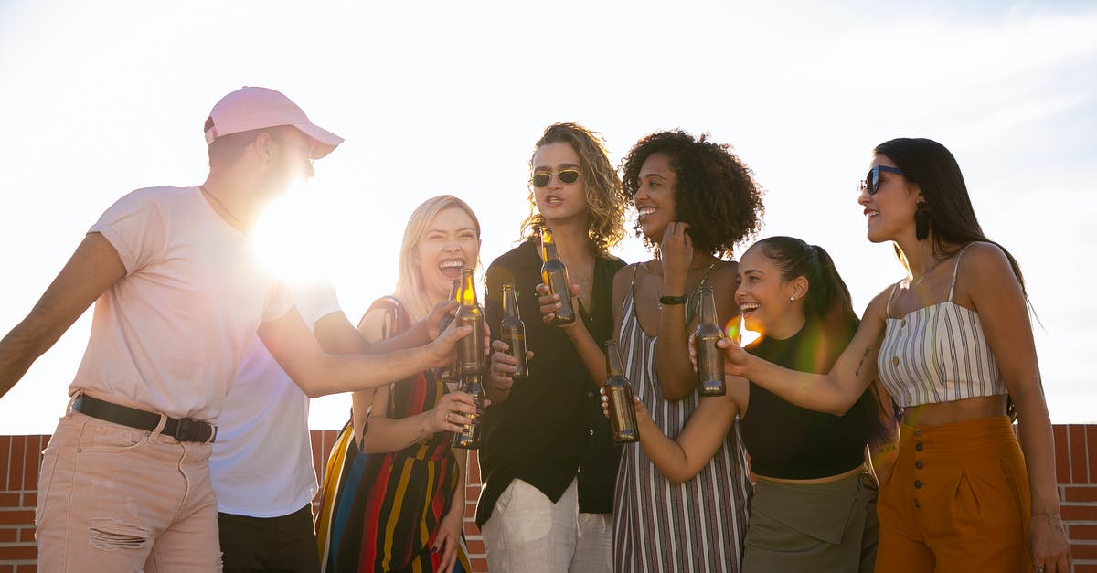 What is the best way to toast pecans? - Group of joyful multiracial friends in summer outfits clinking beer bottles and laughing while gathering together on sunny rooftop