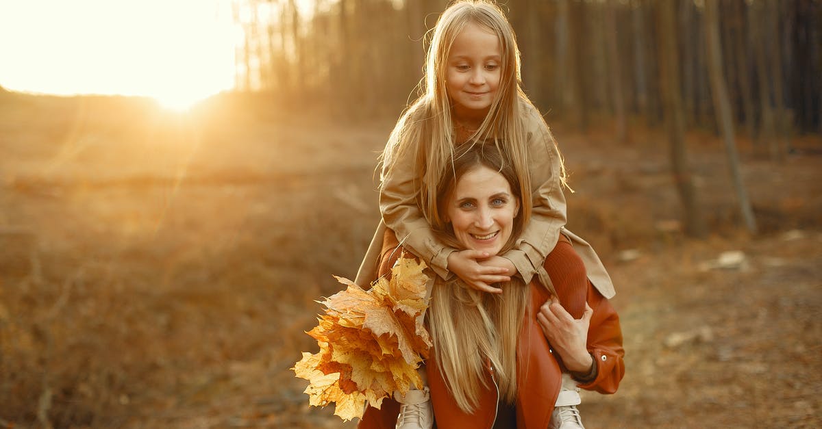 What is the cellular activity behind massaged greens? - Cheerful young woman in casual outerwear with bunch of yellow leaves carrying on shoulders daughter while walking in autumn park on sunset