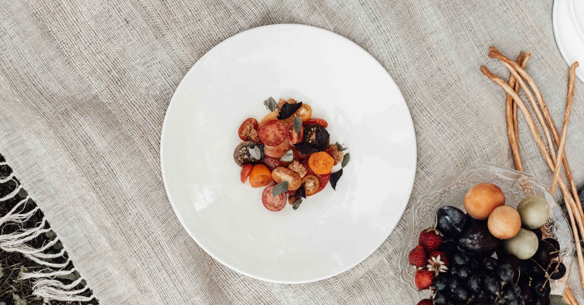 What is the conversion rate between plum tomatoes and "regular" tomatoes? - Top view of vegetarian fresh salad with various tomatoes and herbs on plate near bowl with strawberries and grapes near nectarines and straws on picnic blanket near grass in daytime