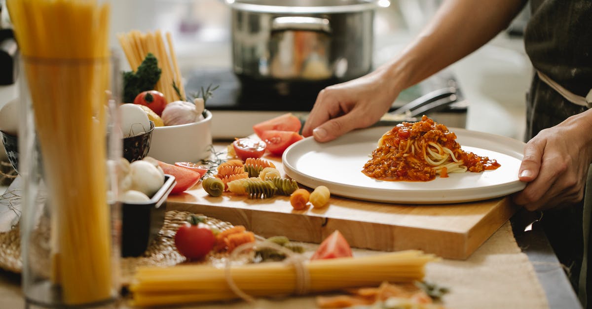 What is the correct timing when cooking spaghetti sauce from minced meat and prepared tomato sauce? - Crop anonymous cook standing at table with various ingredients and cooking pasta with meat and tomatoes