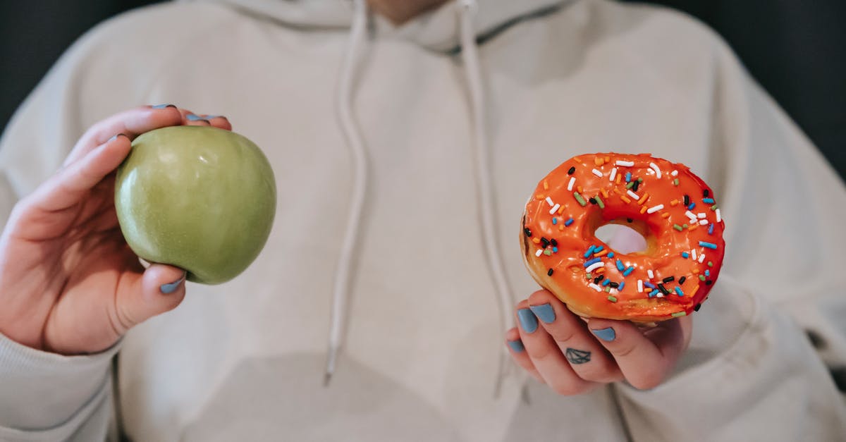 What is the difference between doughnut and krapfen? - Crop faceless woman demonstrating ripe green apple and sweet doughnut