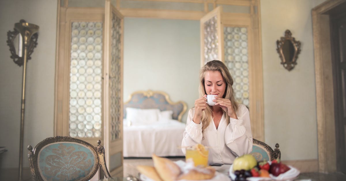 What is the difference between expensive wine and regular wine? - Glad female in elegant wear sitting at table with metal tray of healthy breakfast in vintage hotel room and drinking coffee in morning