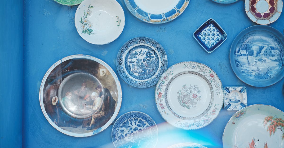 What is the difference between these tableware flatware and cutlery? - Assorted vintage plates of different sizes and ornaments hanging on bright blue wall in light studio