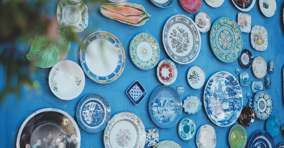 What is the difference between these tableware flatware and cutlery? - Collection of various ceramic plates of different sizes and ornaments arranged on bright blue wall in studio