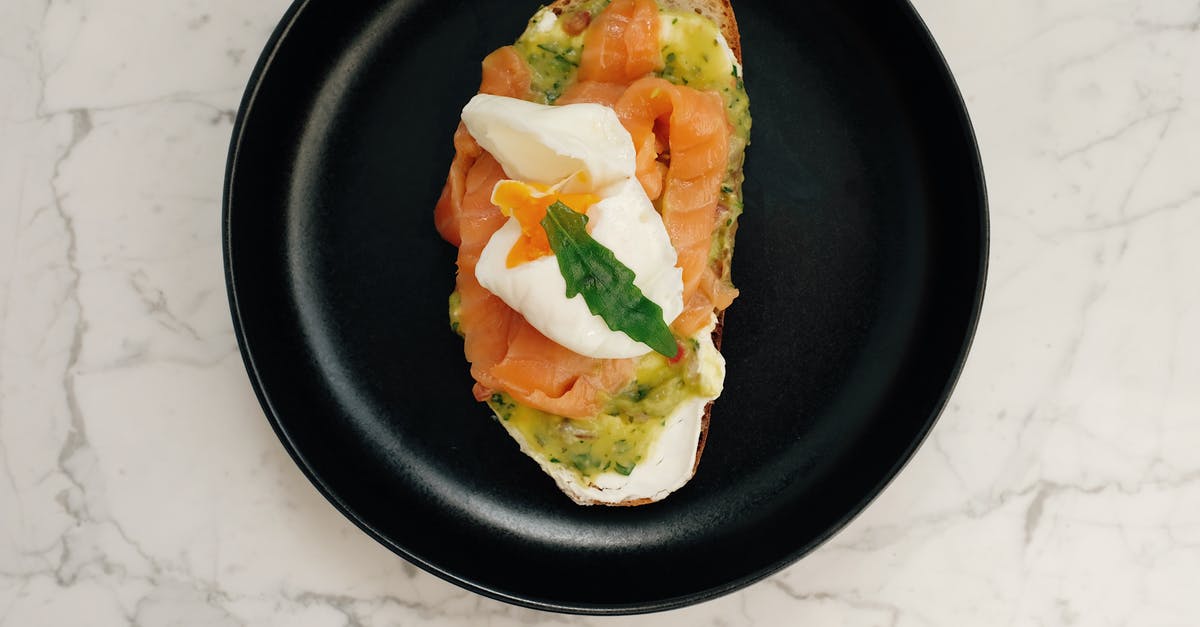 What is the effect of poaching fish in milk? - Top view of black ceramic plate with tasty toast with salmon and poached egg served on white marble table