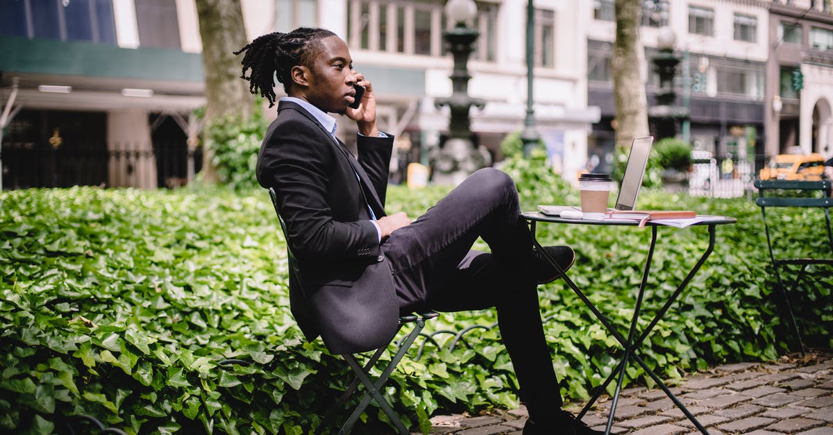 What is the formal definition of savory? - Side view serious African American businessman in black formal wear sitting at table in city park with legs crossed and having conversation via modern smartphone