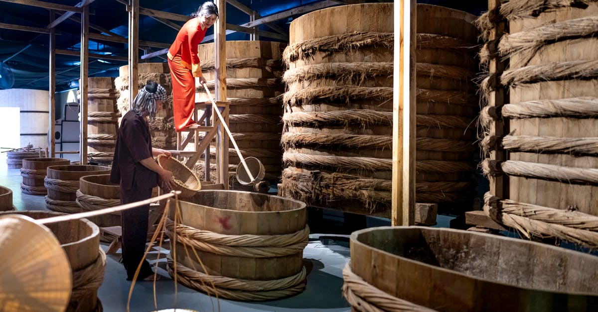 What is the origin of fish sauce in asia? - Factory employees with wooden buckets near barrels with ropes in fish sauce factory