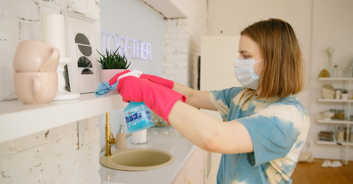 What is the preferred method for sanitizing the kitchen? - Woman Wearing Face Mask While Cleaning the Kitchen